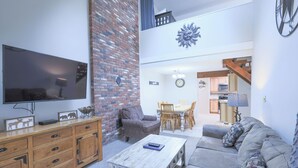 Una sala de estar con televisor, un mueble de madera, un sofá gris y un comedor con mesa y sillas.