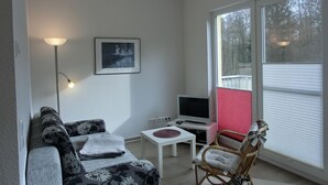 Un salon avec un canapé, un fauteuil, une petite table, un téléviseur et un tableau accroché au mur.