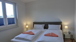 Un lit double avec deux oreillers, une table de chevet avec une lampe et une fenêtre avec des stores.