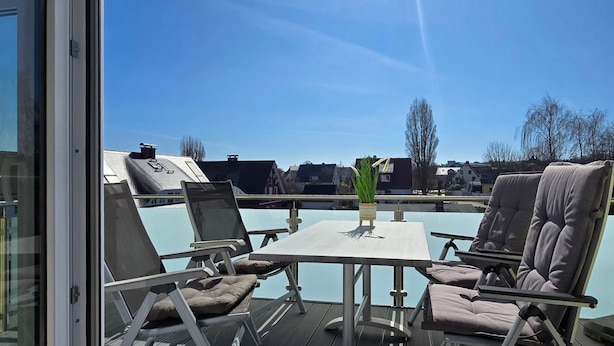 En tagterrasse med et bord og stole, en lille plantekasse og udsigt over kvarteret.