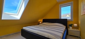 Ein Schlafzimmer mit einem Bett, zwei Nachttischen, einem Fenster und einem Oberlicht.