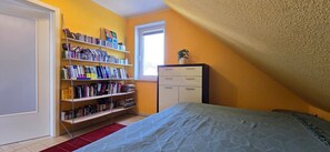 Um quarto com uma cama, uma estante, uma cômoda e uma janela.