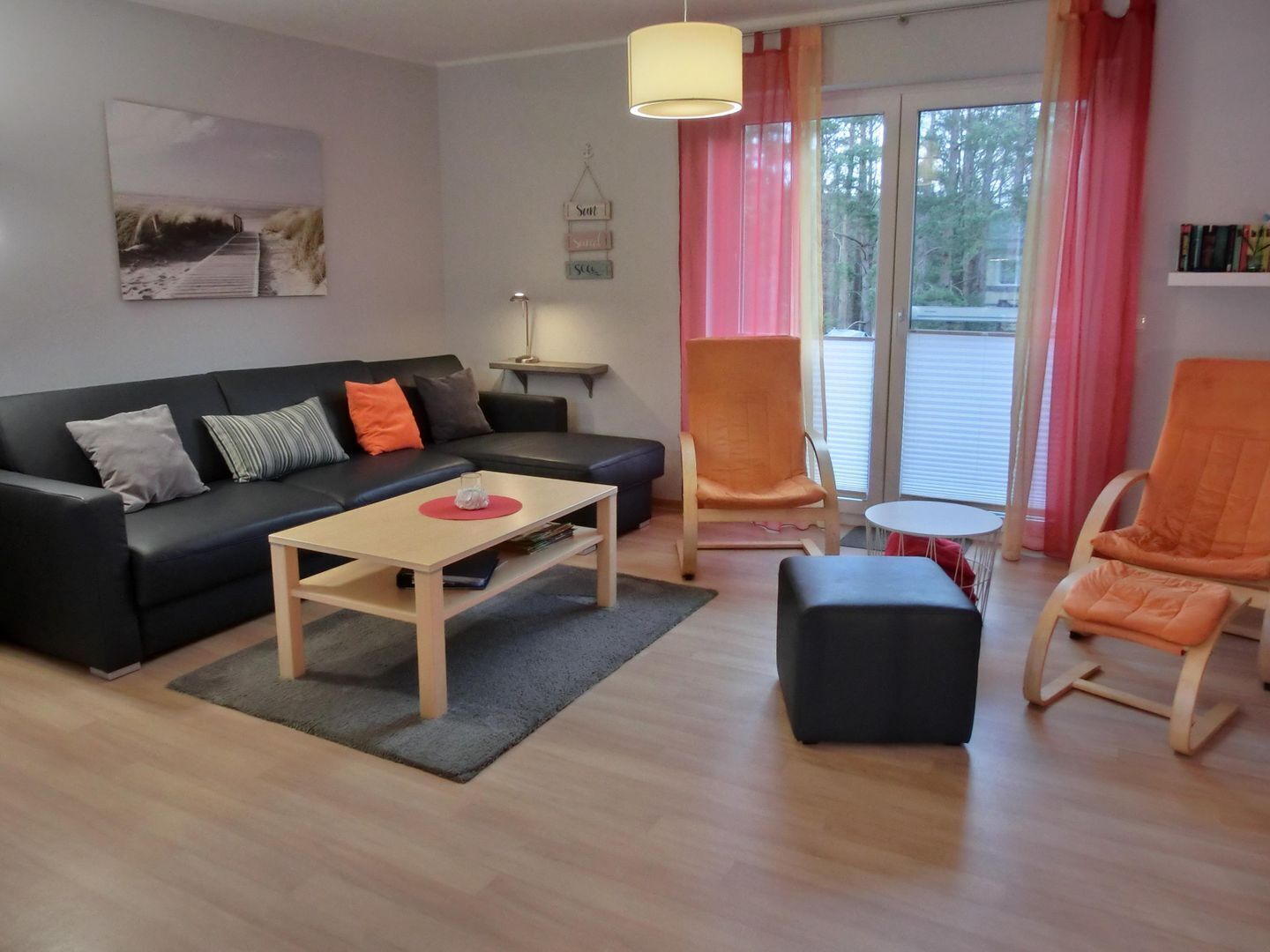 Ein modernes Wohnzimmer mit einem schwarzen Sofa, einem Holztisch und zwei orangefarbenen Sessel.