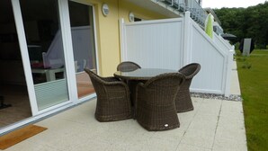 An outdoor patio with wicker furniture, a glass door, and a white fence.