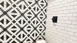 A bathroom with a geometric patterned wall, a white tiled floor, and a wooden bench with a towel.