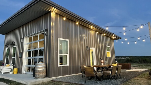 A modern building with large windows, a patio with outdoor seating, and string lights.