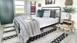 A bedroom with a bed, a wardrobe, a bedside table with a plant, a window, and a wall-mounted picture.