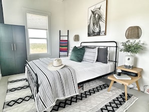 Relax in a serene bedroom with a large bed, striped blanket, and a beautiful view of lush greenery outside.