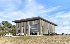 Situated on a grassy area, this single-story building features a symmetrical facade with a grid of windows and a covered outdoor seating area.