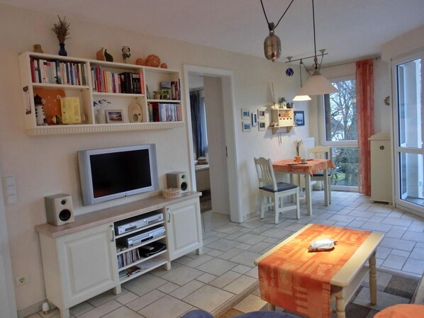 A living room with a TV, bookshelf, and dining area.