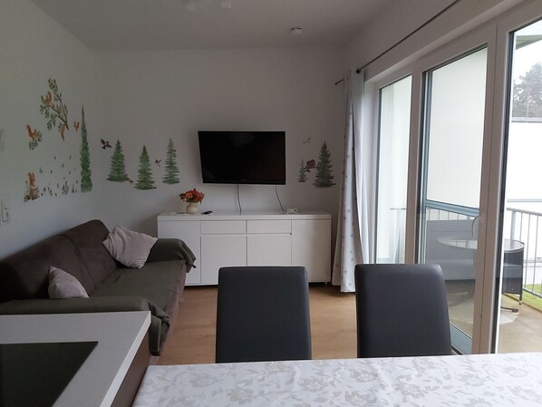 A modern living room with a sofa, a dining table, and a TV mounted on the wall.