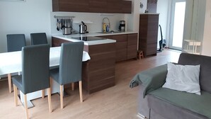 A modern kitchen with a central island, dining area with chairs, and a living space with a sofa. - Apartment KWi 26 OG - 2-room apartment for 3 pers. WLAN (Gelbensande)