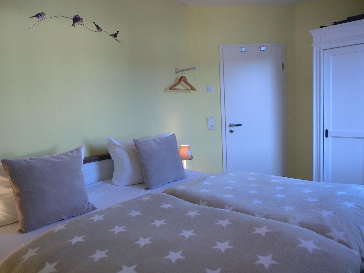 Une chambre avec deux lits, une porte, un luminaire fixé au mur et un élément décoratif mural.