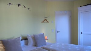 A room with two beds, a door, a wall-mounted light, and a wall decoration. - Apartment KWi 26 OG - 2-room apartment for 3 pers. WLAN (Gelbensande)