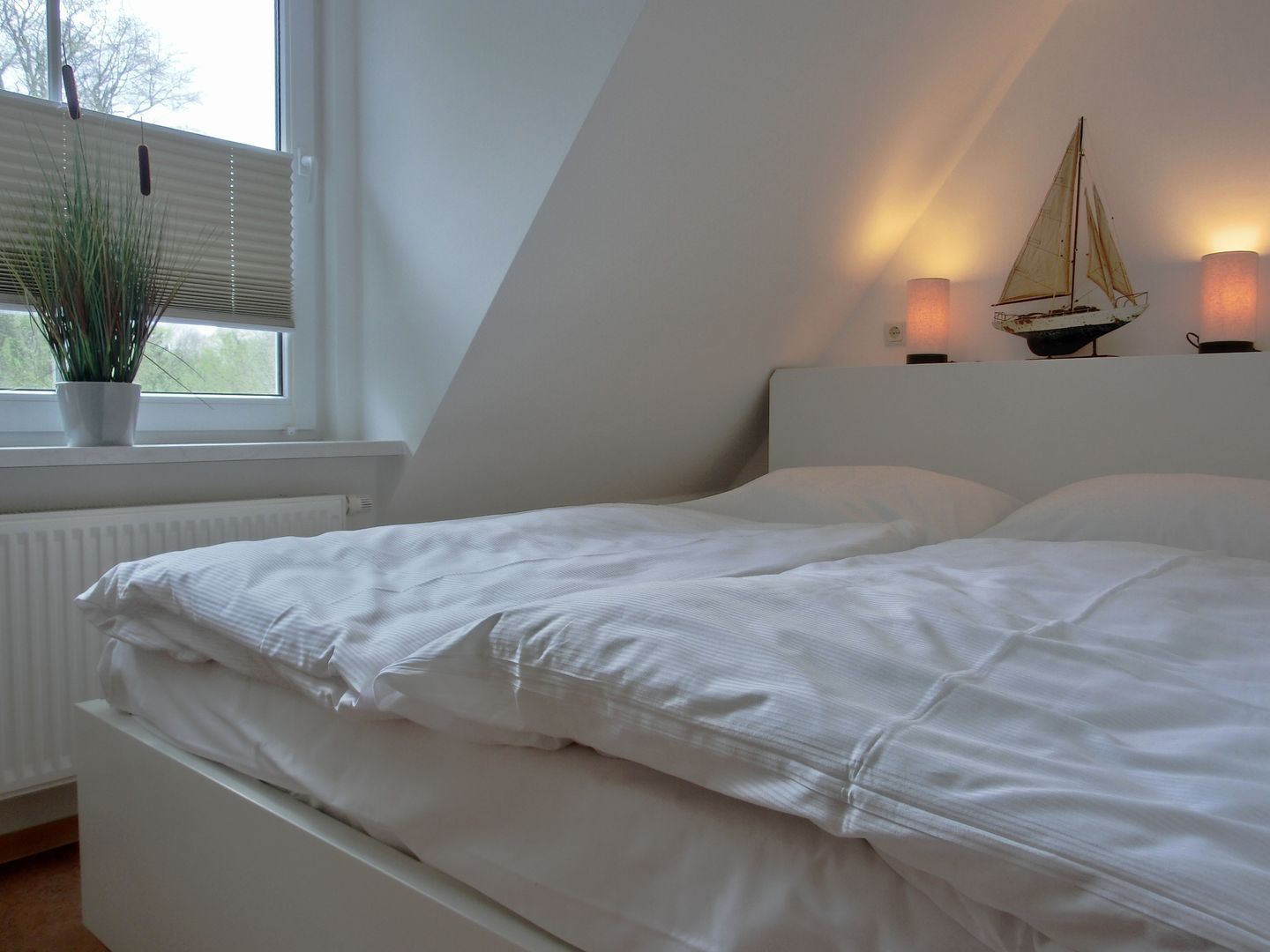 A bedroom with a bed, a window with blinds, a potted plant, and wall-mounted lights.