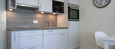 A modern kitchen with white cabinets, a built-in oven, a microwave, and a clock on the wall.