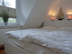 Une chambre à coucher avec un lit, une fenêtre avec des stores, une plante en pot et des lampes fixées au mur.