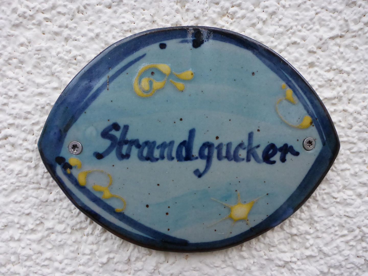 A round ceramic plate with the word "Strandgucker" and abstract yellow designs.