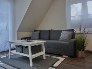 Un salon moderne avec un canapé gris, une table basse blanche et une plante dans un panier tressé.