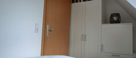 Quarto com cama, guarda-roupa e pequeno armário.