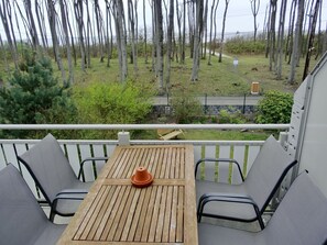 Un balcon avec une table en bois et deux chaises, donnant sur un espace verdoyant agrémenté d’arbres et d’un sentier.