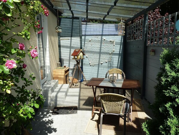 A covered patio with a table and chairs, a small dog, and a birdhouse.