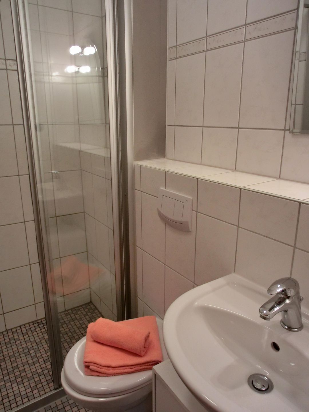 A bathroom with a glass shower enclosure, a white sink with a chrome faucet, and a toilet with a pink towel on top.