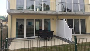 Ein zweistöckiges Gebäude mit Balkon, großen Fenstern und Außenbestuhlung.