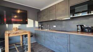 Eine moderne Küche mit Flachbildfernseher, Holztisch, Barhocker, grauen Schränken und einer Siemens Dunstabzugshaube.
