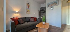 A modern living room with a grey sofa, red cushions, a wooden coffee table, and a wall-mounted clock.