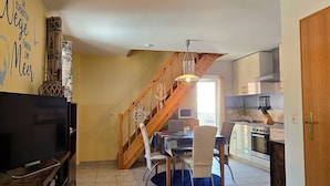 Una sala de estar moderna con un televisor de pantalla plana, una escalera de madera, un comedor con mesa y sillas, y una cocina con estufa y microondas.