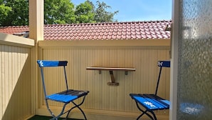 Un porche cubierto con dos sillas plegables azules y una mesa de madera.