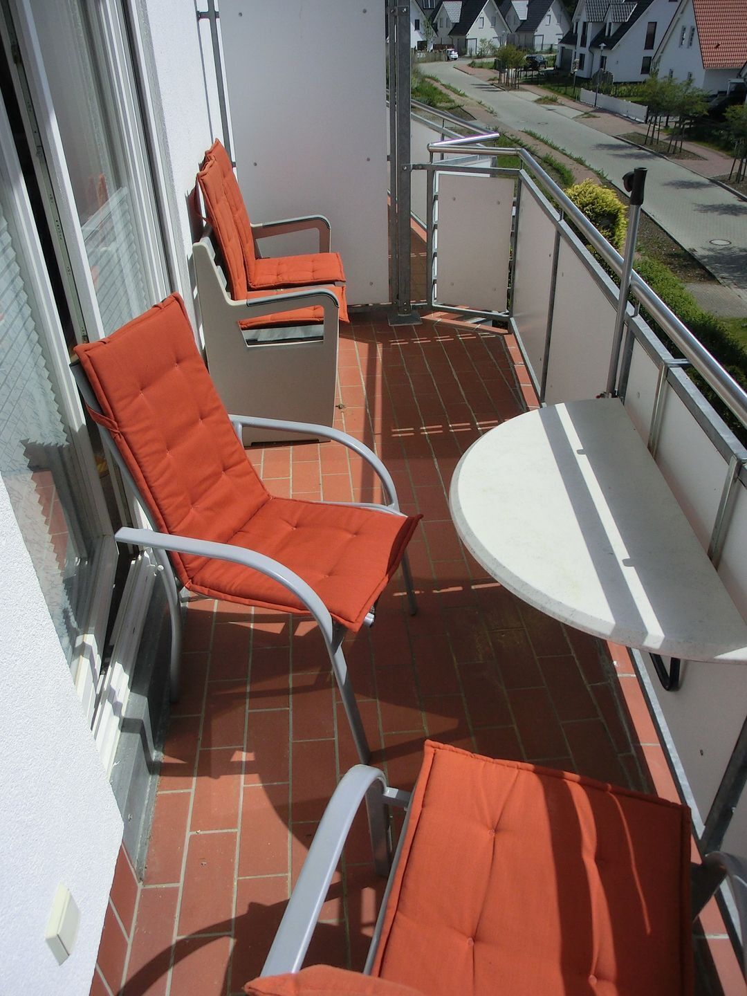 A balcony with two orange cushioned chairs and a small white table.