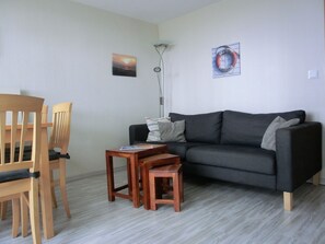 A living room with a wooden chair, a small wooden table, a grey sofa, and a floor lamp.