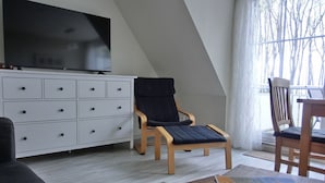 Una sala de estar moderna con un televisor de pantalla plana, una silla de madera, un sofá y una mesa de comedor.