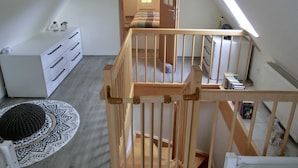 Un dormitorio estilo loft con escalera de madera, cómoda blanca, alfombra estampada y tragaluz.