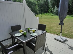 A patio table with chairs, a white fence, and a grassy yard.