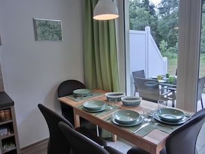 Un comedor con una mesa de madera dispuesta para cuatro, platos verdes y una lámpara colgante.