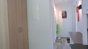 Un pasillo con un armario de madera, una puerta blanca, un objeto verde y una ventana pequeña.