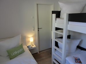 A bunk bed room with a bedside table, a lamp, and a green pillow.