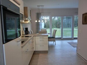 A modern kitchen with a large window, a dining area with a chair, and a coffee maker.