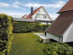 Um imóvel residencial com gramado bem cuidado, deck de madeira e um edifício branco com telhado de telhas vermelhas.