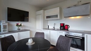 A compact kitchen with a dining area, a flat-screen TV, a coffee maker, and a microwave. - Apartment KWV 1 ground floor - 2-room apartment for 3 pers. on the ground floor and garden (approx. 30 m²) (Graal-Müritz)