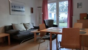 Moderni olohuone, jossa on sohva, ruokapöytä tuoleineen, lattiavalaisin ja ikkuna, jossa on verhot.