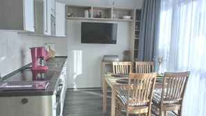 A modern kitchen with a dining area, wooden chairs, and a flat-screen TV mounted on the wall. - Apartment KWi 77 OG "Windflüchter" - 2-room apartment for 3 persons on the upper floor with (Graal-Müritz)