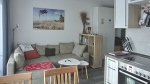A modern living room with a sofa, a small table, and a kitchen area with a stove. - Apartment KWi 77 OG "Windflüchter" - 2-room apartment for 3 persons on the upper floor with (Graal-Müritz)