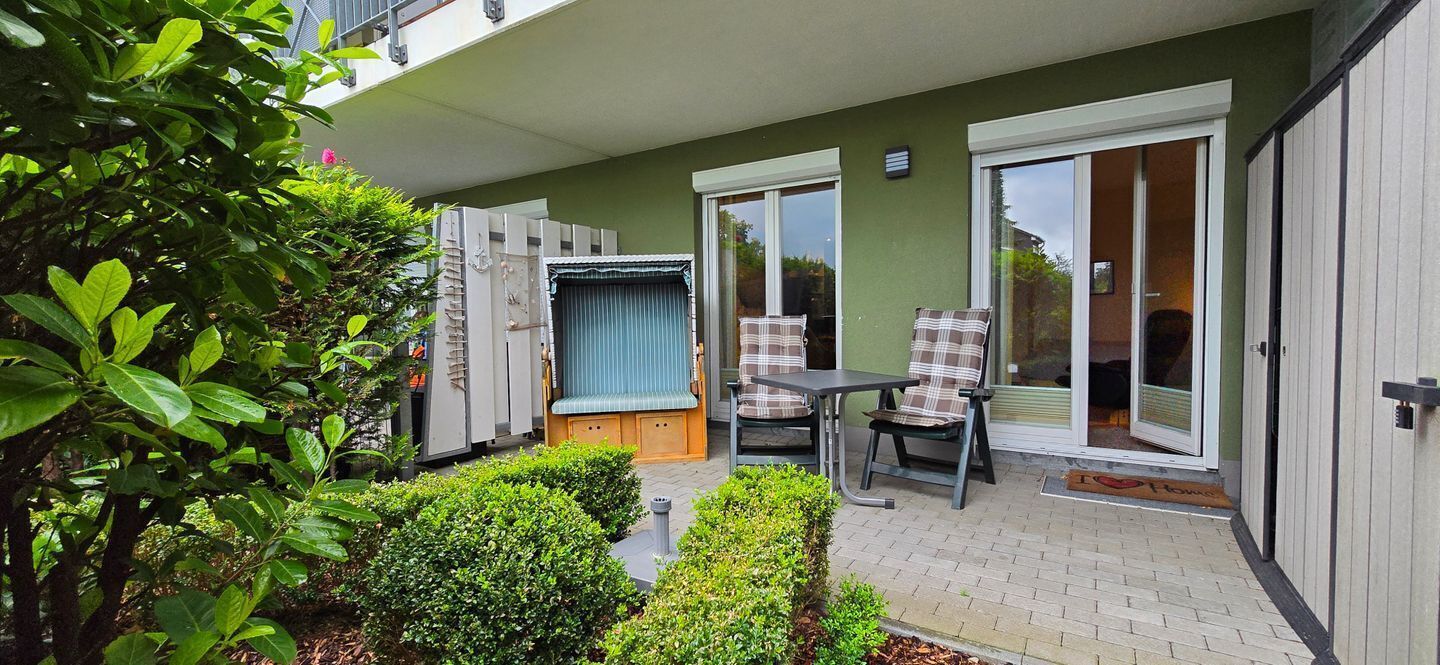Eine Terrasse mit Tisch und Stühlen, eine Schiebetür und ein kleiner Gartenbereich.