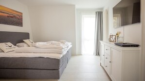 Una camera da letto moderna con un divano letto grigio, un comodino bianco con un portatile e un'ampia finestra con tende.