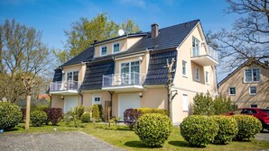 Un edificio residenziale a due piani con un balcone, un garage e un giardino curato.