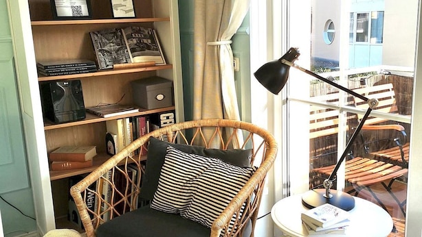 Un rincón acogedor para leer con una silla de mimbre, una mesita redonda y una estantería llena de libros y adornos.